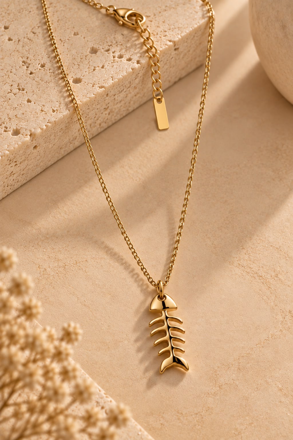 Collar Marea con colgante dorado de espina de pez apoyado sobre piedra beige