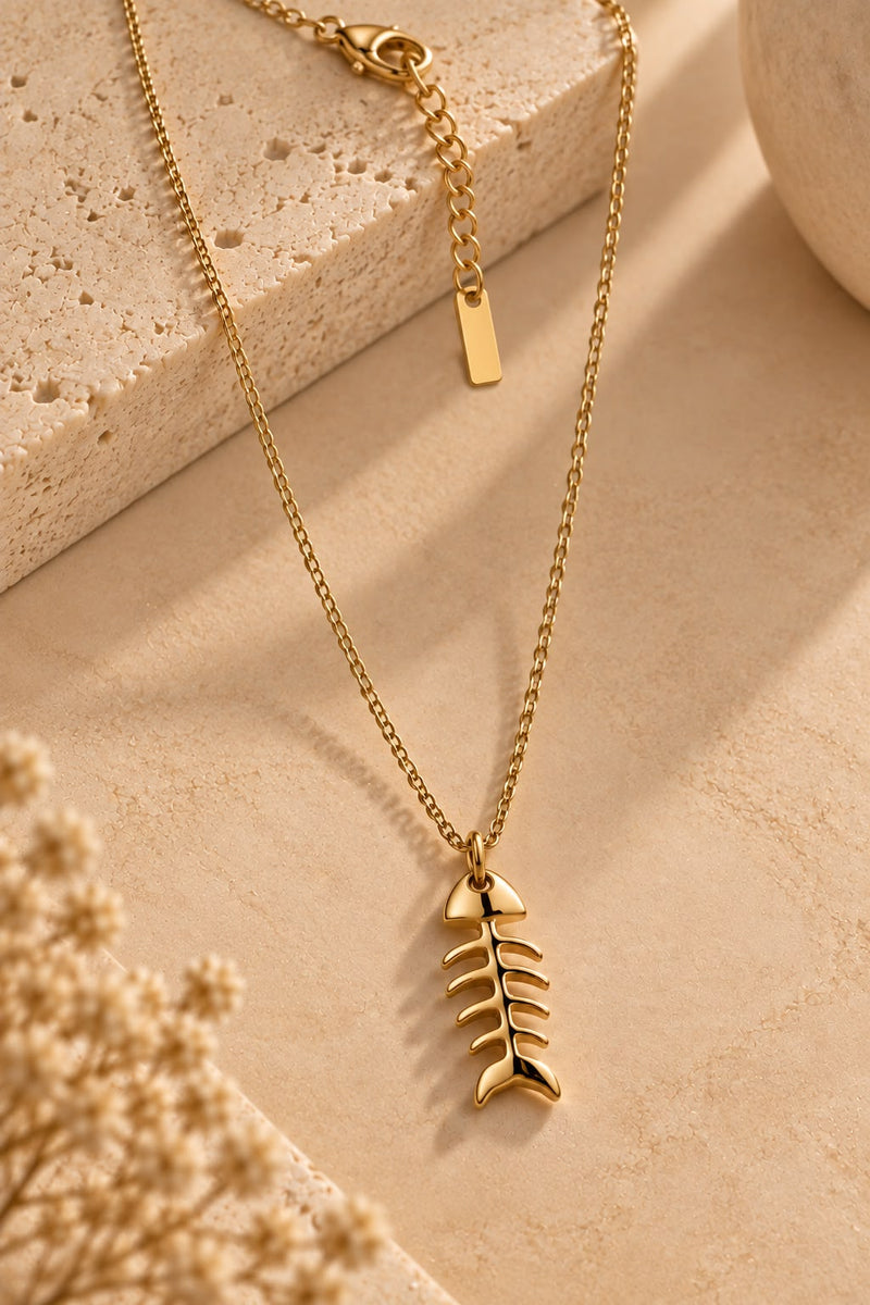 Collar Marea con colgante dorado de espina de pez apoyado sobre piedra beige