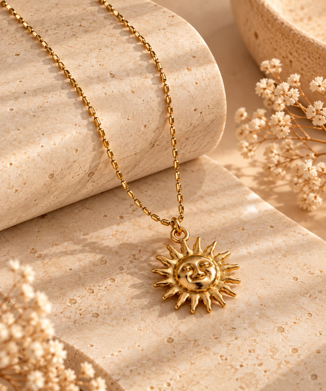 Collar Sol Dorado sobre piedra beige, con su colgante de sol y la cadena de bolitas