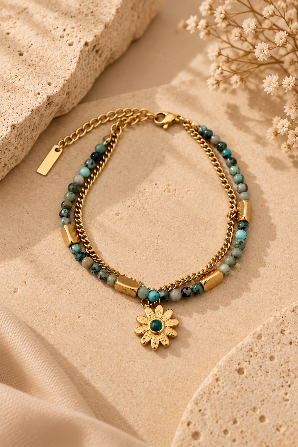 Pulsera Alma Verde sobre piedra beige, con su cadena dorada, sus piedrecitas verdes y el colgante de flor