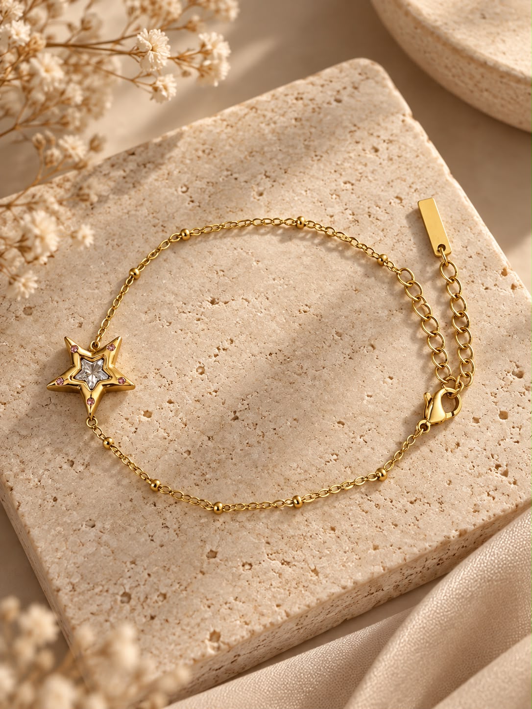 Pulsera Estrellita completa, con su estrella dorada y la cadena fina, sobre piedra beige