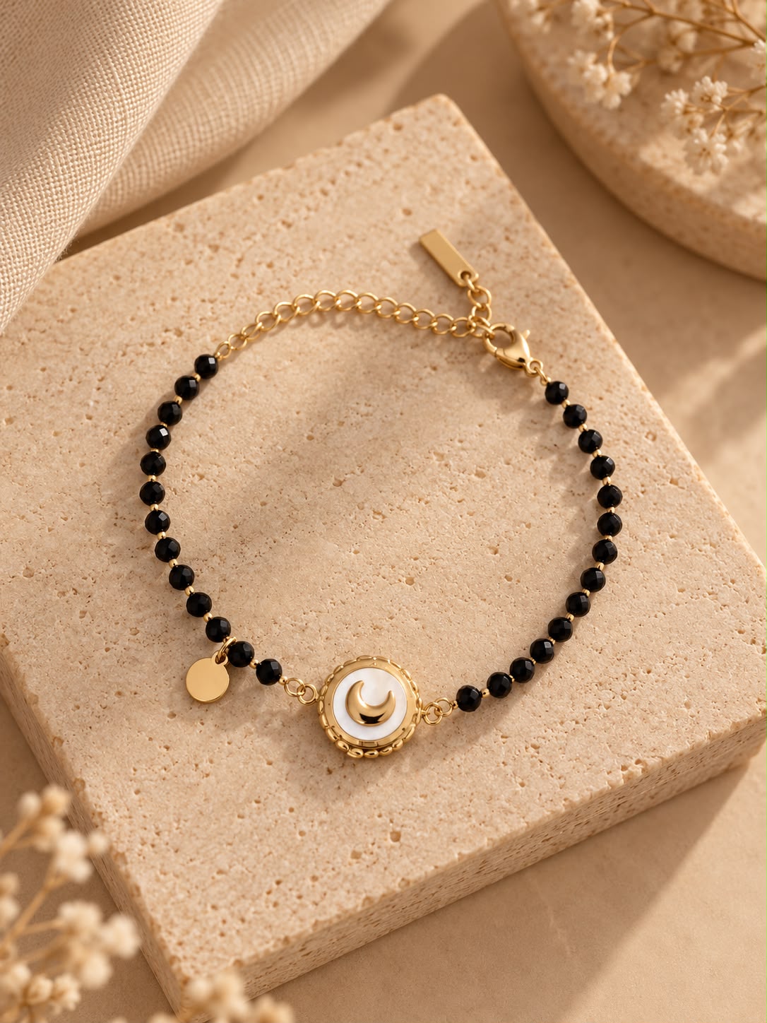 Pulsera Luna Negra con cuentas negras y medallón de luna dorada sobre piedra beige